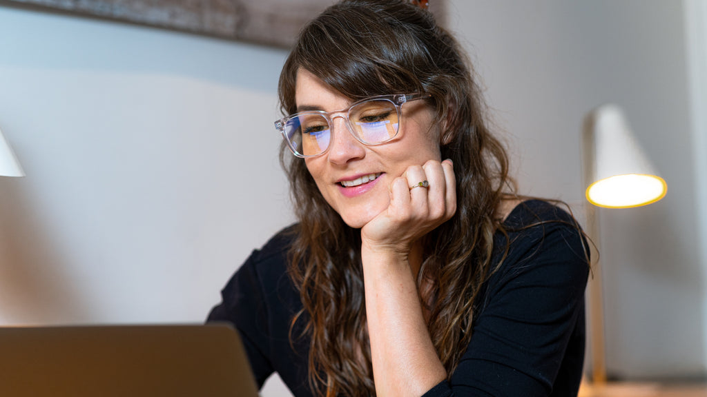 Eine braunhaarige Frau mit schwarzem Oberteil arbeitet mit unserer Blaufilter Brille am Computer. 